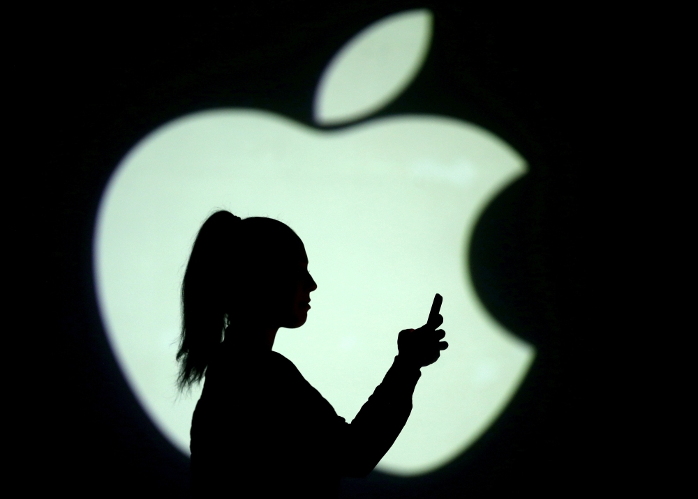 Silhouette of a mobile user seen next to a screen projection of the Apple logo. - Reuters