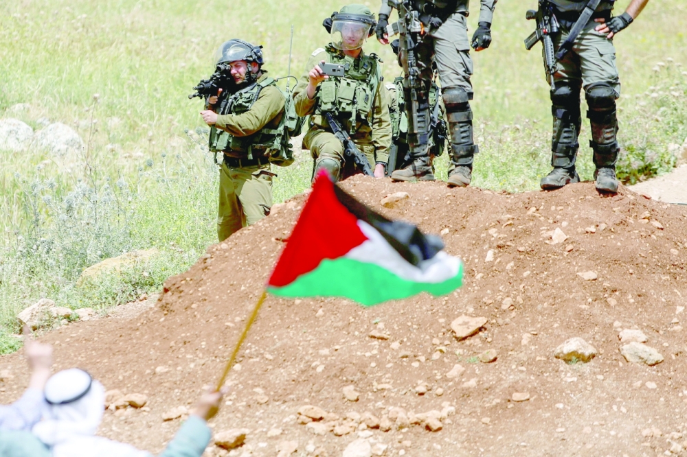 An Israeli soldier aims a weapon as a demonstrator waves a Palestinian flag during a protest against Israeli settlements in the Israeli-occupied West Bank. - Reuters
