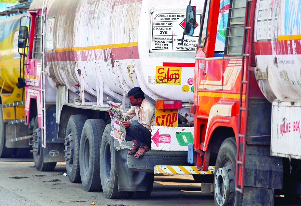 A driver reads a newspaper as he sits on a spare tire attached to a parked oil tanker at a truck terminal in Mumbai. — Reuters