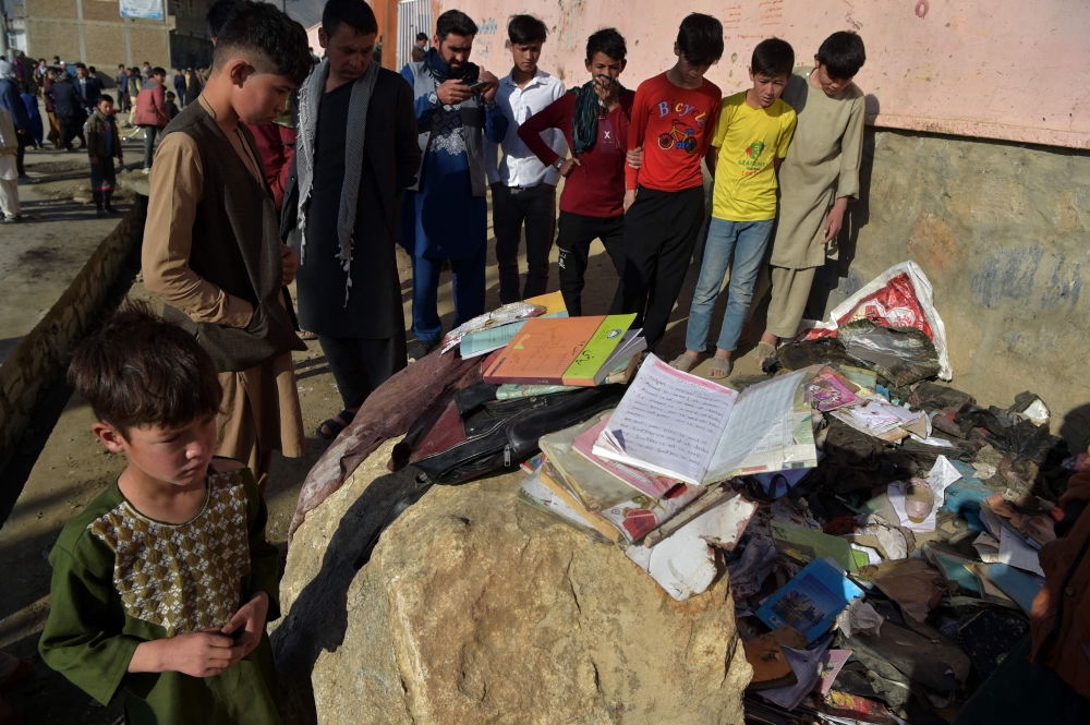 Onlookers stand next to the backpacks and books of victims following multiple blasts outside a girls' school in Dasht-e-Barchi on the outskirts of Kabul. - AFP
