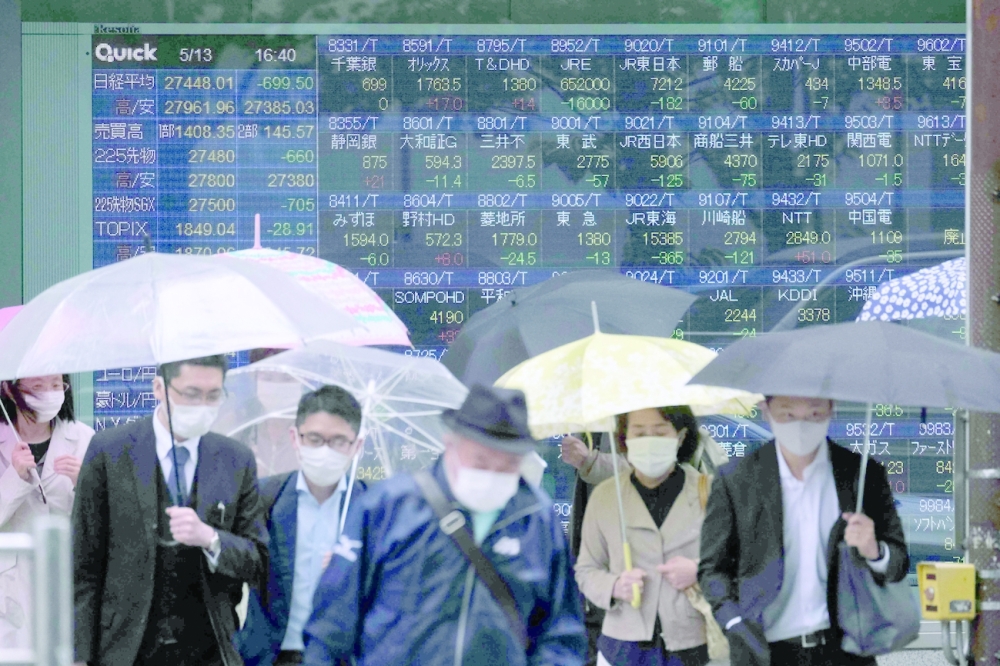Pedestrians cross a road in front of an electronic quotation board displaying the numbers of company stock prices on the Tokyo Stock Exchange in Tokyo. - AFP