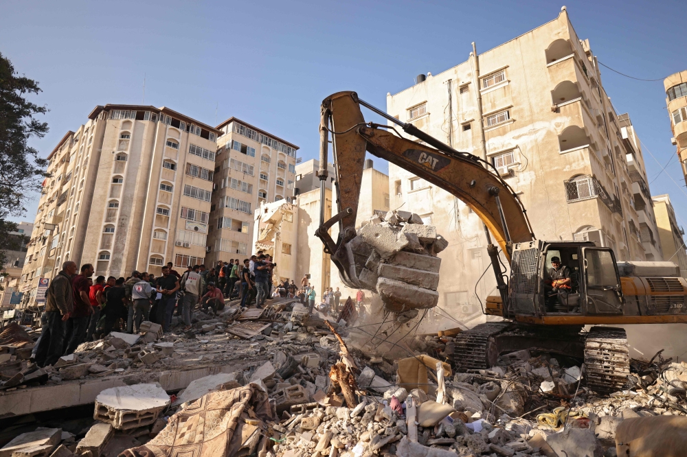 An excavator clears the rubble of a building, after it was struck by Israeli strikes, in Gaza City, May 16, 2021.  Israeli forces pummeled the densely populated Gaza Strip, the sixth day of bombardments on the Palestinian enclave controlled by Islamist group Hamas, which fired back rocket barrages.  / AFP / MOHAMMED ABED

