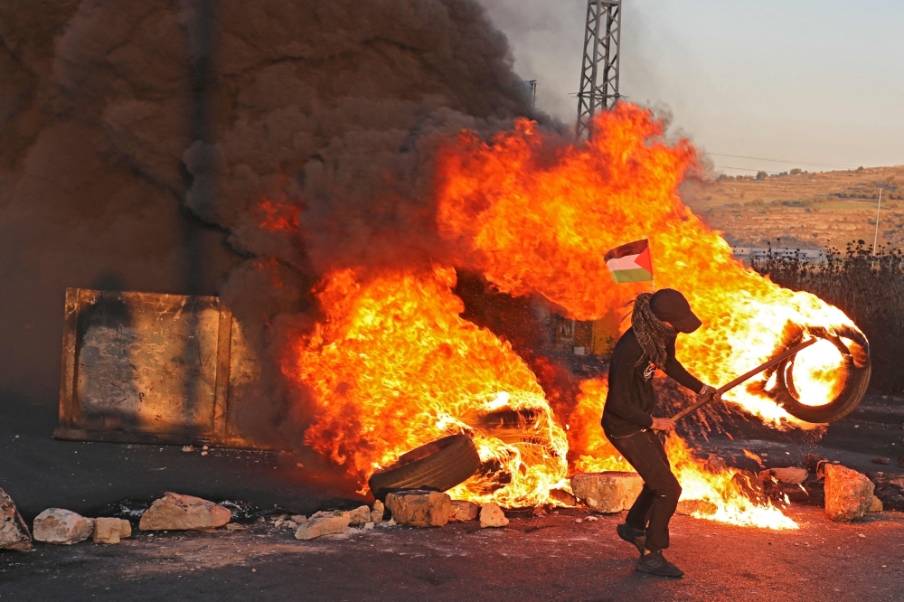 Palestinian demonstrators burn tires during a protest against the tension in Jerusalem and the Israeli-Gaza fighting, on May 17, 2021 in the occupied West Bank, near the settlement of Beit El next to Ramallah. / AFP / ABBAS MOMANI


