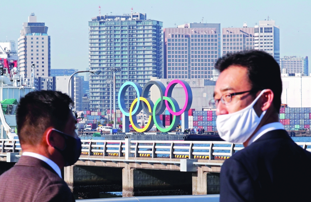 Men wearing face masks watch as giant Olympic rings are transported for reinstallation at the waterfront area at Odaiba Marine Park in Tokyo. — Reuters