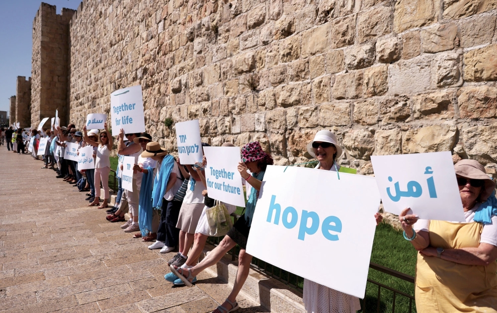 People display signs as they take part in an event calling for coexistence and an end to violence amid Israel-Gaza fighting, along a section of Jerusalem’s Old City walls, on Wednesday. — Reuters