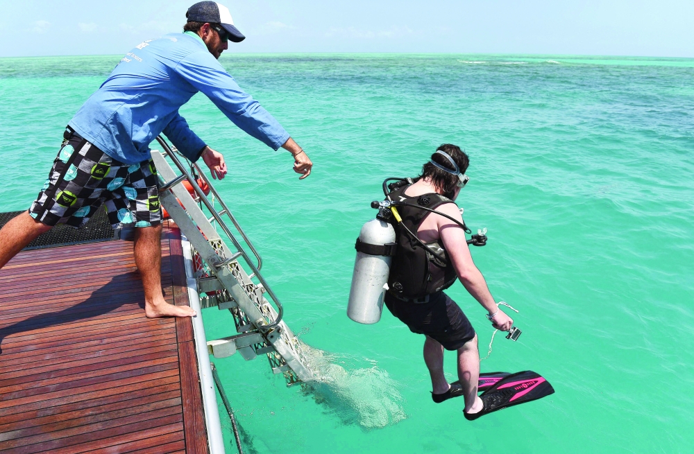 A  scuba-diving tourist on the Ocean Freedom dive boat helped into the water by a crew member on Australia's Great Barrier Reef. - AFP File Photo
