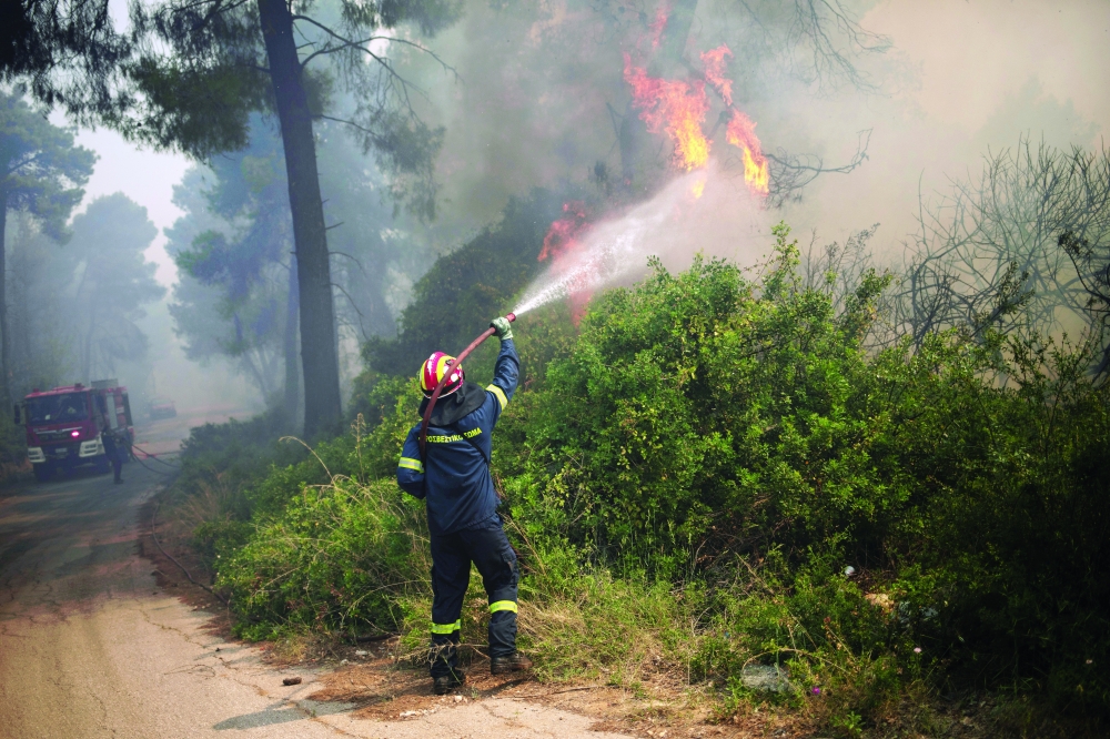A firefighter tries to extinguish a fire burning in the village of Mazi, near Corinth, Greece. - Reuters