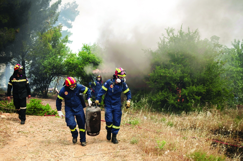 Firefighters carry a gas tank away from a wildfire burning in the village of Mazi, near Corinth, Greece. - Reuters