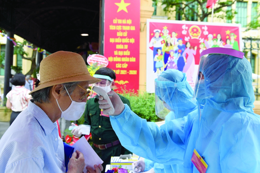A medical worker checks the temperature of a voter at a polling station in Hanoi. - AFP