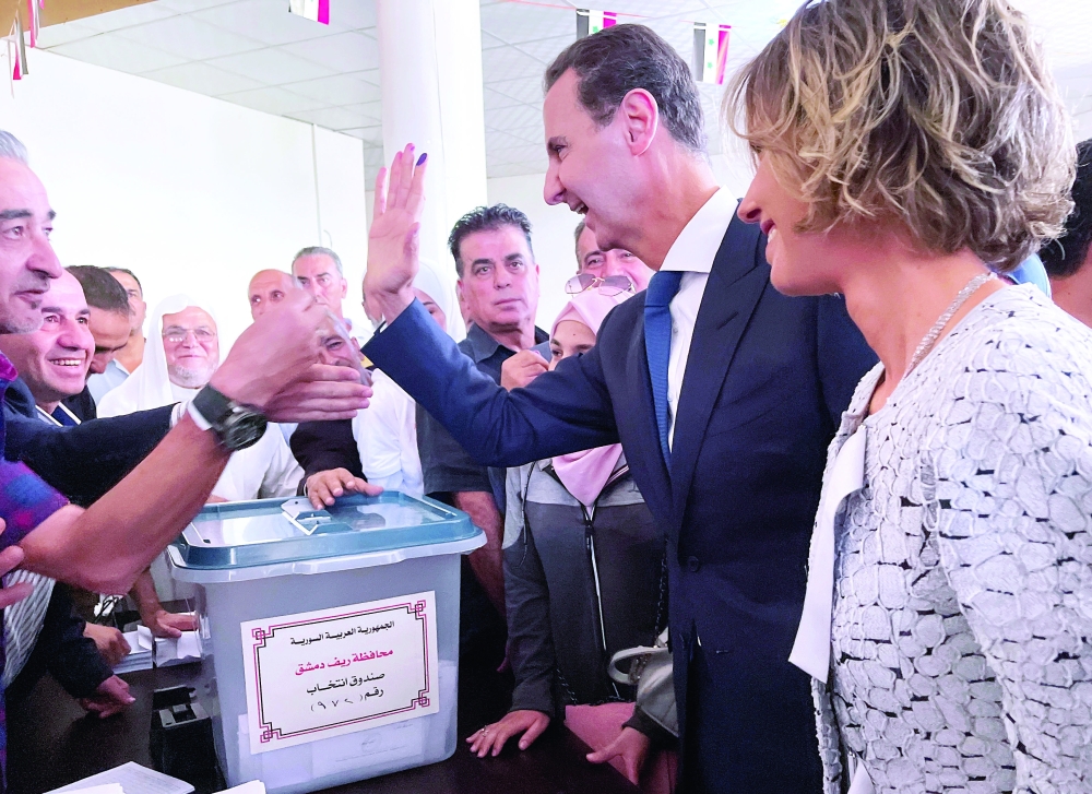 President Bashar al Assad and his wife Asma greet supporters after casting their votes in the country's presidential elections at a polling station, in Douma, on Wednesday. — Reuters 