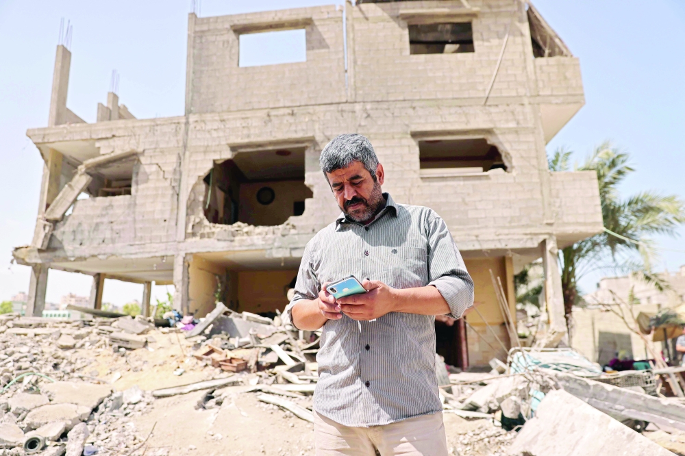 A Palestinian, who now lives with his family in a school run by the United Nations, stands in front of his house, damaged during the recent Israeli bombing in Gaza City, on Saturday. - AFP