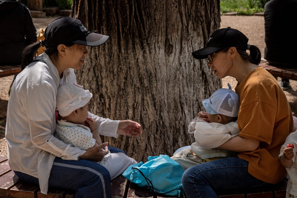 Two women and two babies sitting on a bench in a park in Beijing. China has relaxed its family planning policy to allow couples to have three children after a census showed its population is rapidly ageing.