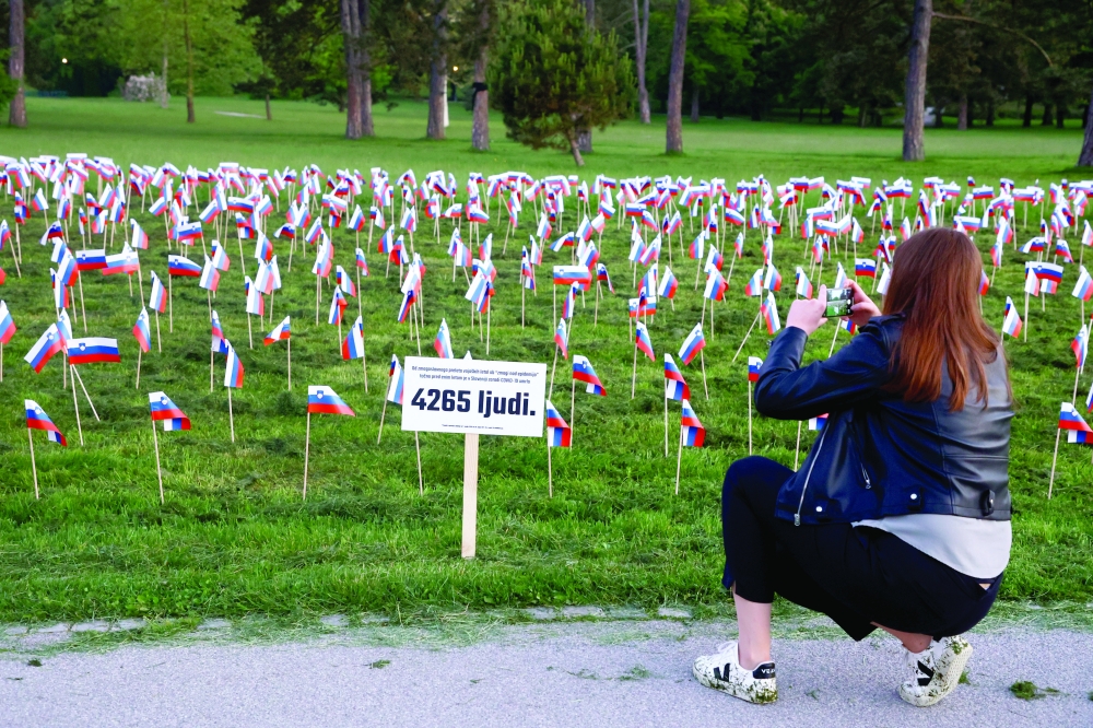 A woman takes photographs of flags planted by protesters in tribute to those who have died of the coronavirus disease, a year after the Slovenian government called an official end to its coronavirus epidemic, in Ljubljana, Slovenia on Tuesday. The sign indicates that 4,265 people have died in the year since the announcement. — Reuters
