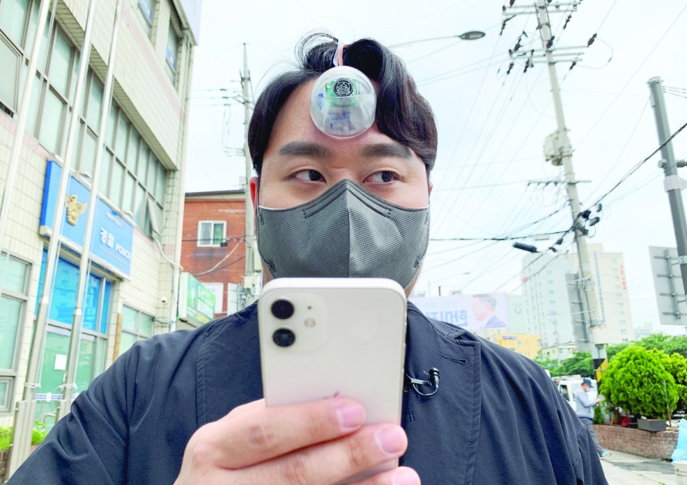 South Korean industrial designer Paeng Min-wook showcases a robotic eye, called 'The Third Eye', on his forehead as he uses his mobile phone while walking on street, in Seoul. - Reuters 