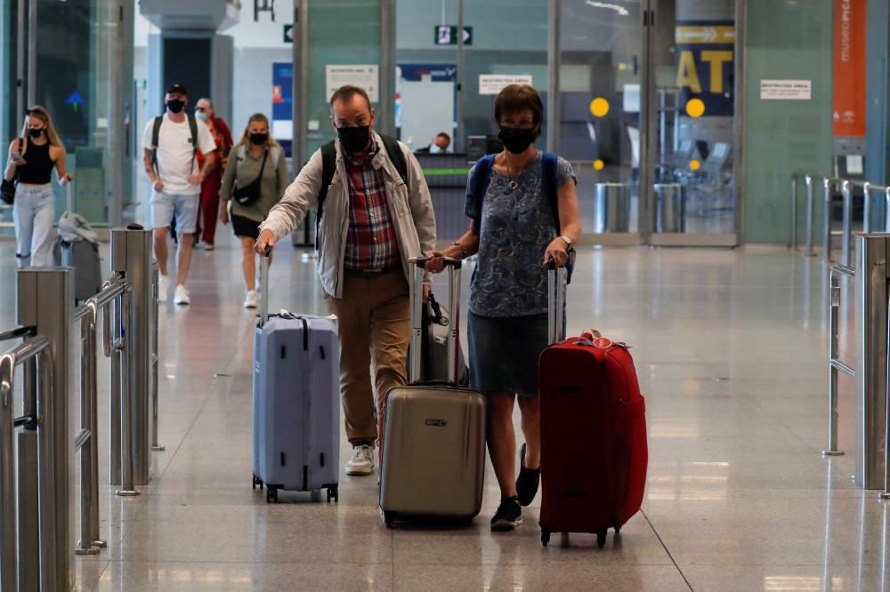 Tourists wearing protective face masks walk with their luggage as they arrive at Malaga-Costa del Sol Airport, in Malaga, Spain, on Monday. — Reuters