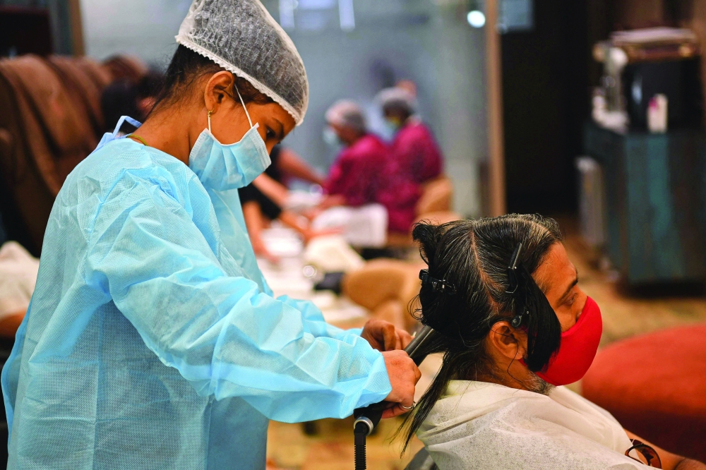A staff member wearing protective gear attends a customer after personal grooming services were allowed to resume at a hair saloon in Mumbai. - AFP