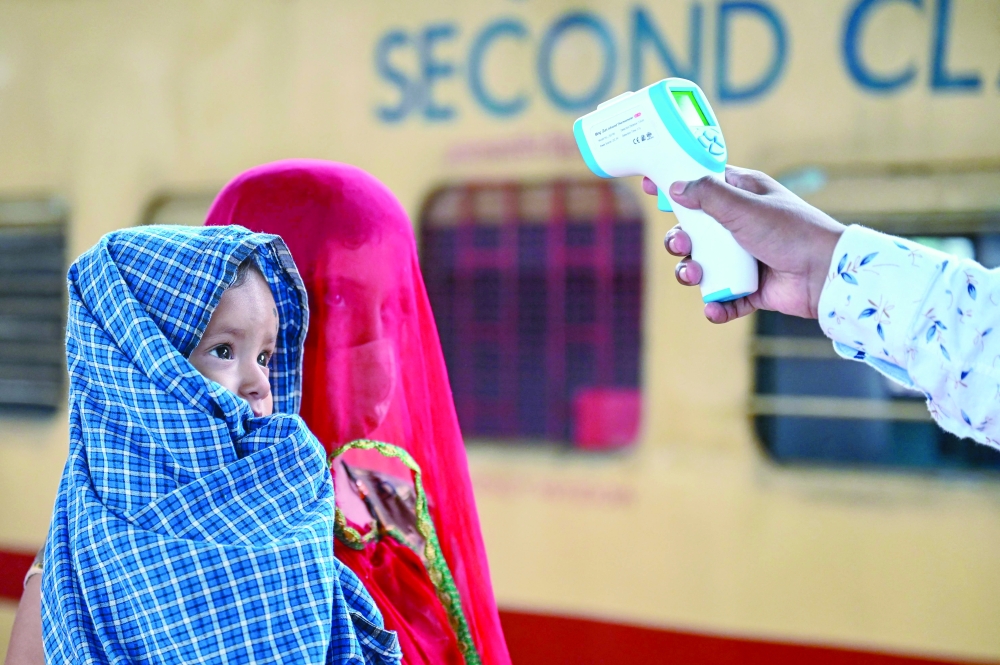 A health worker checks the body temperature of a passenger during a Covid-19 screening as she arrives with her child at a railway platform on a long distance train, in Mumbai on Tuesday. - AFP 