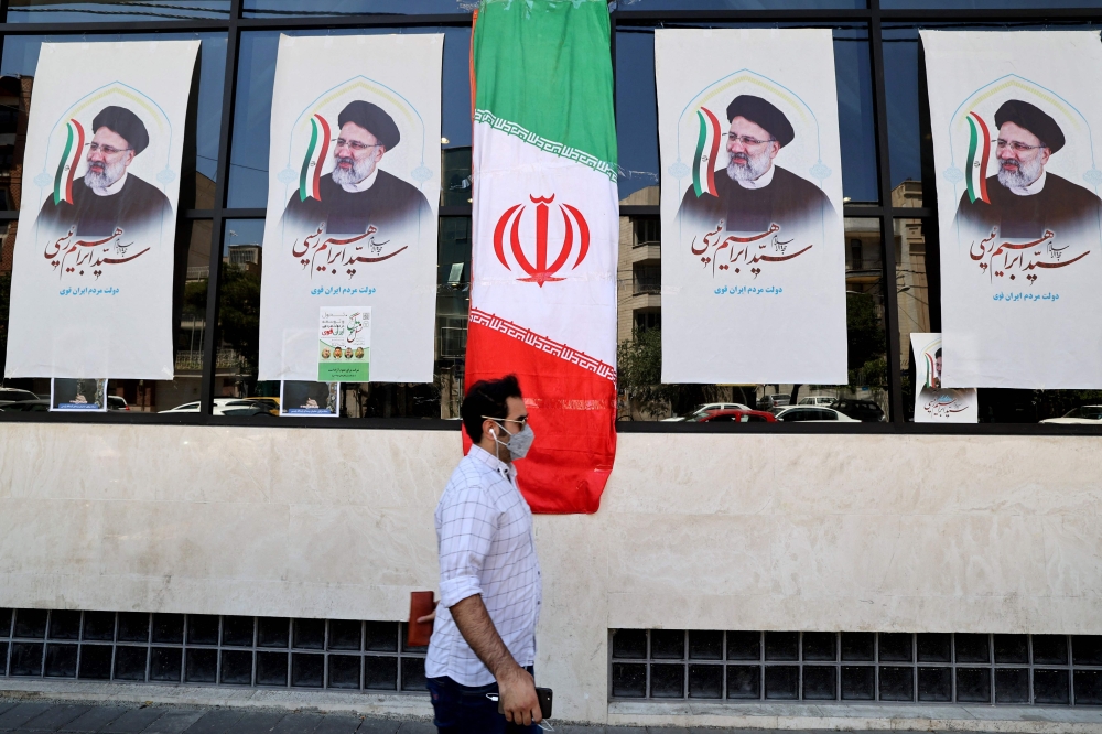 An Iranian man walks by posters of presidential candidate Ebrahim Raisi outside a campaign office in Tehran. - AFP