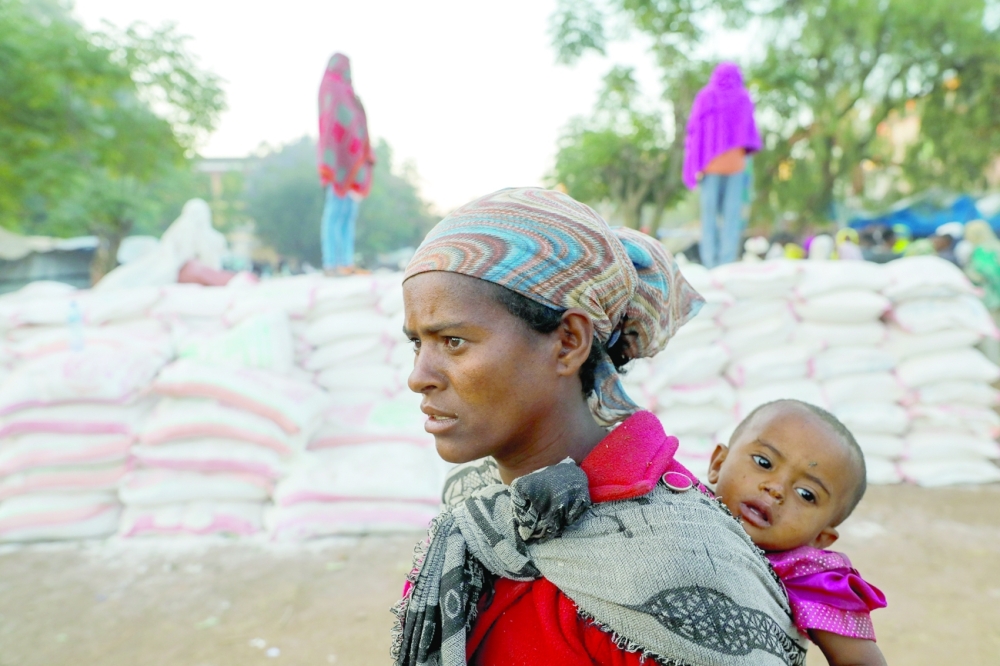 A woman carries an infant as she queues in line for food, at the Tsehaye primary school, which was turned into a temporary shelter for people displaced by conflict, in the town of Shire, Tigray region, Ethiopia. Reuters
