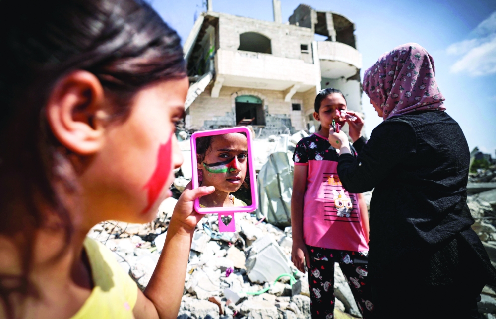 A Palestinian woman paints a national flag on the face of a child amidst the rubble of buildings destroyed by last month’s Israeli bombardment of the Gaza Strip in the northern part of the Palestinian enclave. — AFP