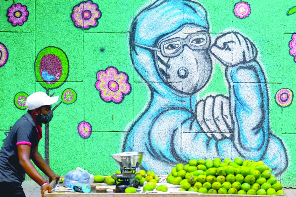 A fruit vendor pulls his cart as he walks past a wall mural depicting a frontline coronavirus worker wearing a face mask in New Delhi. - AFP 