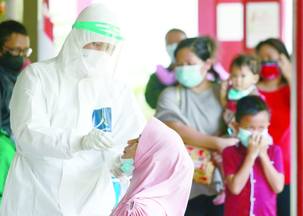 A healthcare worker in personal protective equipment takes a swab sample from a woman to test for Covid-19 during mass testing at a school in Jakarta, on Friday. - Reuters