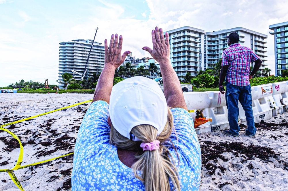 A woman prays as rescue workers search the rubble at the site of the partially collapsed 12-story Champlain Towers South condo building in Surfside, Florida. - AFP