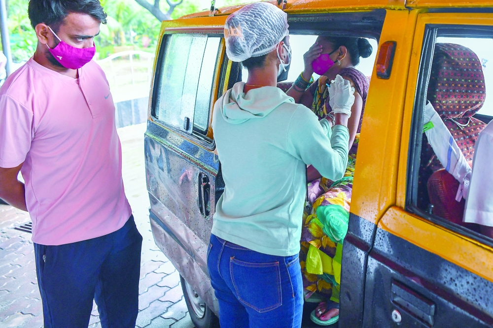 A youth looks at a healthcare worker as she inoculates his mother sitting inside a taxi with a dose of the Covishield vaccine at a drive-in vaccination facility in Mumbai on Tuesday. - AFP 
