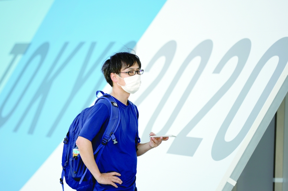 A man wearing a face mask stands in front of Tokyo 2020 Olympic Games signage at the Main Press Center. -- Reuters