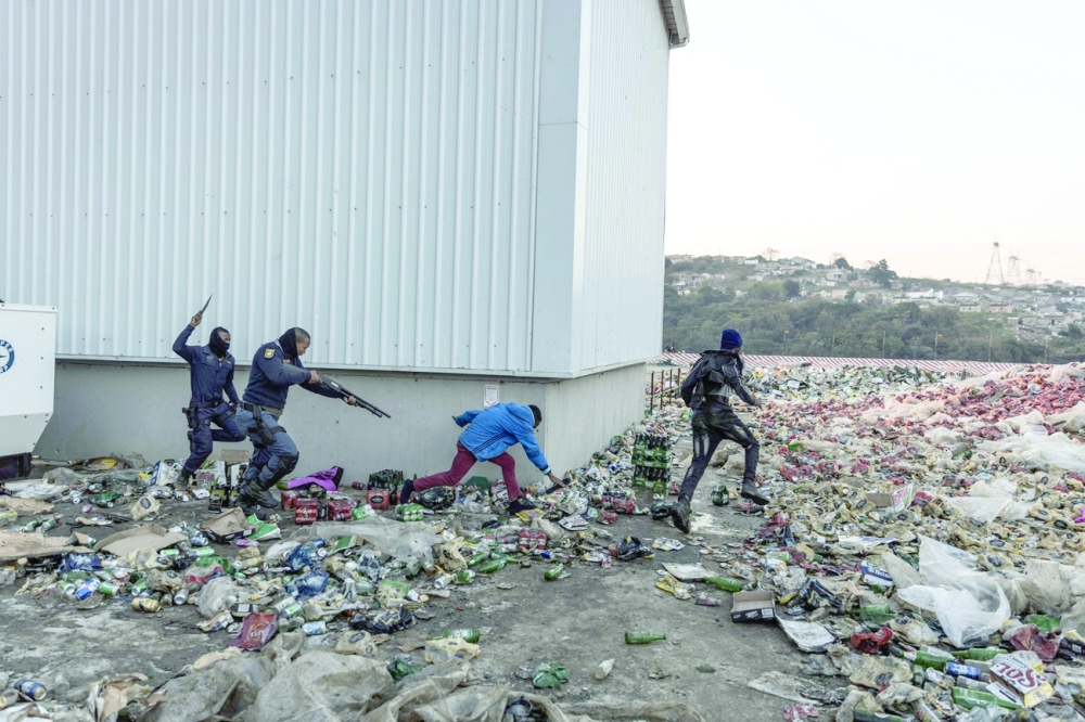 Two members of SAPS chase and shoot rubber bullets at two suspected looters outside a warehouse storing alcohol in Durban on Friday. - AFP 