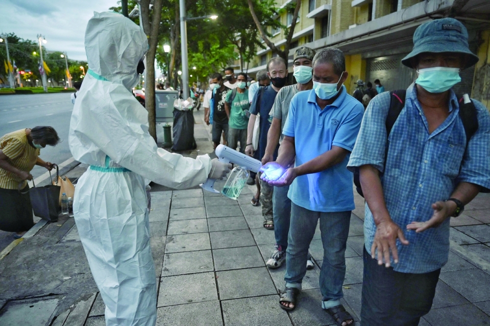 A volunteer wearing protective gear sanitizes the hands of a man as homeless and low-income residents stand in a queue to receive daily food donations near Democracy Monument amid Covid-19 pandemic in Bangkok. - AFP