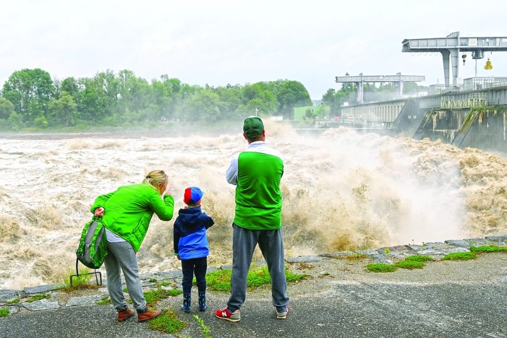 A family watches the agitated waters of the river Inn at the barrage of Ranshofen in Braunau am Inn, Austria, following heavy rainfall causing damaging floods. - AFP