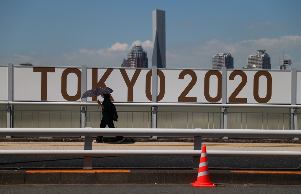 A woman shelters from the sun under an umbrella as she walks past Olympics signage. -- Reuters