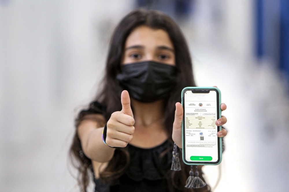 A Kuwaiti teenager holds her phone showing off her Covid-19 vaccination certificate after receiving her shot of the Pfizer-BioNTech vaccine, at a vaccination centre in Kuwait City on Monday. Kuwait this week began offering vaccinations to children aged 12-15 ahead of the start of the school year in September. - AFP
