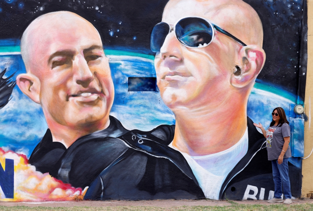 Margarita Moilina of El Paso, poses next to a mural depicting billionaire American businessman Jeff Bezos and his brother Mark (L) in the nearby town of Van Horn, Texas. - Reuters