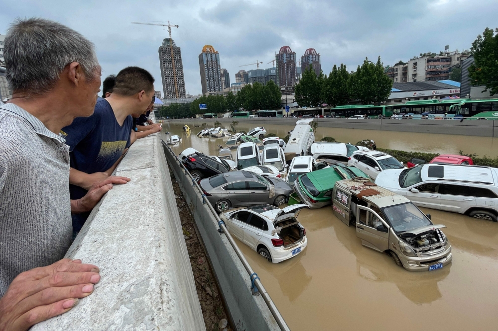 People look out at cars sitting in floodwaters after heavy rains hit Zhengzhou in China's central Henan province. - AFP