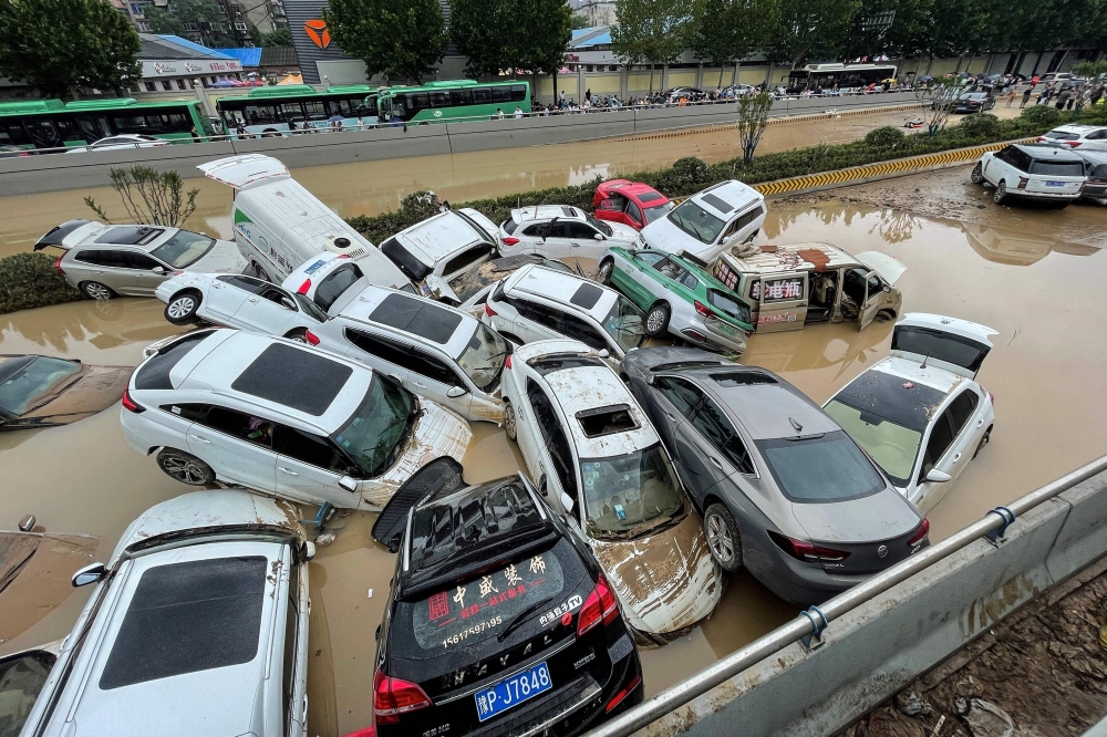 People look out at cars sitting in floodwaters after heavy rains hit Zhengzhou in China's central Henan province. - AFP