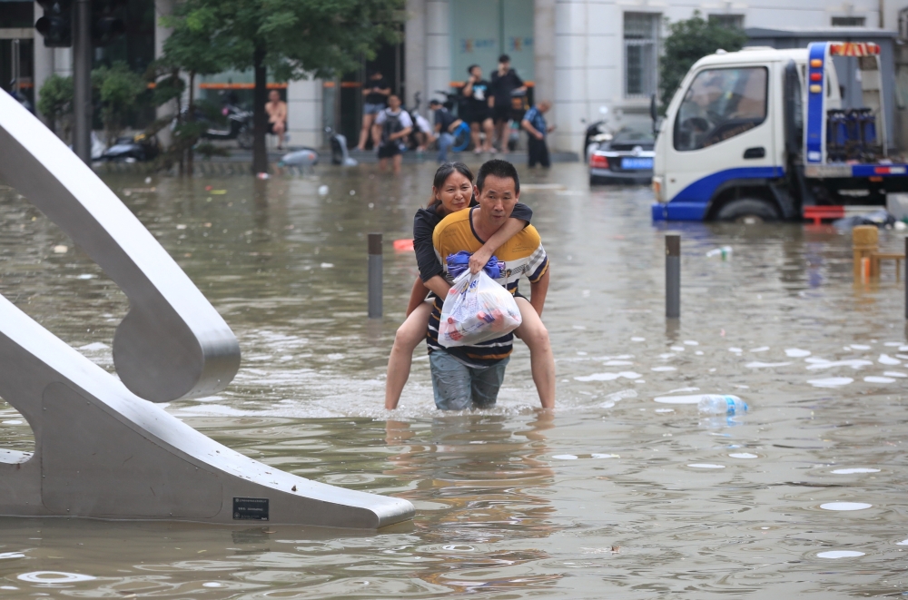 A man carrying a woman wades through a flooded road following heavy rainfall in Zhengzhou, Henan province. - Reuters