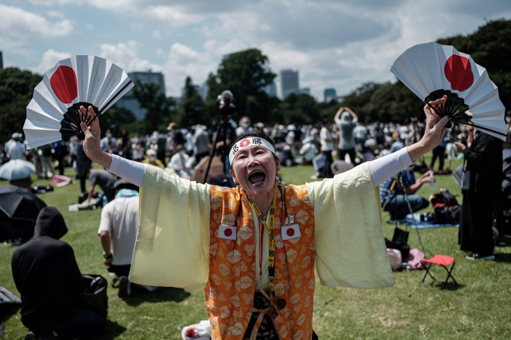 Olympic super-fan Kyoko Ishikawa (C), who has attended every Summer Olympics in the past 30 years, expresses her gratitude as Blue Impulse, Japan's Air Self Defense Force (JASDF) aerobatic team, performs a display to form the Olympic rings in the skies over Tokyo on July 23, 2021. -- AFP