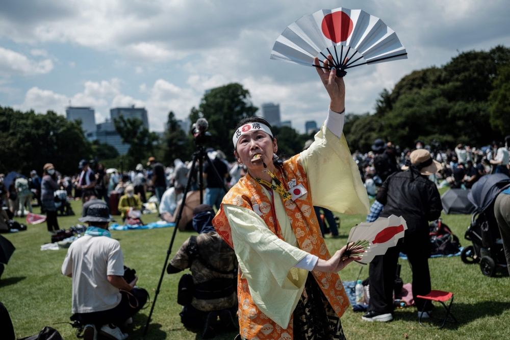 Olympic super-fan Kyoko Ishikawa (C), who has attended every Summer Olympics in the past 30 years, express her gratitude as Blue Impulse, Japan's Air Self Defense Force (JASDF) aerobatic team, performs a display to form the Olympic rings in the skies over Tokyo. -- AFP