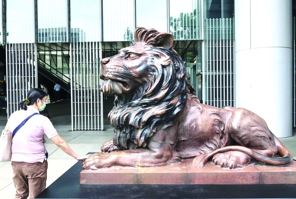 A woman touches a lion sculpture outside HSBC office in Hong Kong. — AFP