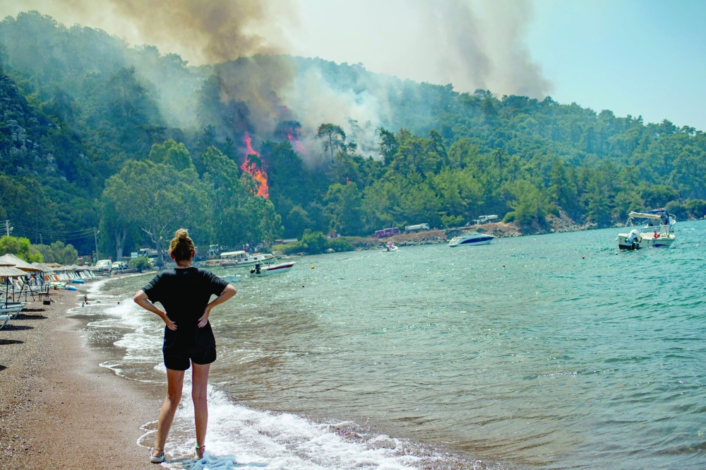 A woman watches from a beach the forest burning on Tuesday in Mugla, a Marmaris’ district, as Turkey struggles against its deadliest wildfires in decades. — AFP