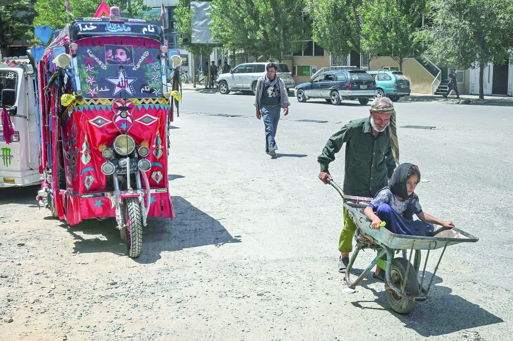 A child sits on a wheelbarrow as a man pushes it past an auto-rickshaw parked along a road in Kabul. - AFP