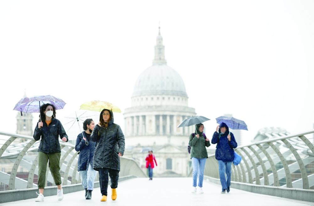 People walk over Millennium Bridge during rainfall in London. - Reuters