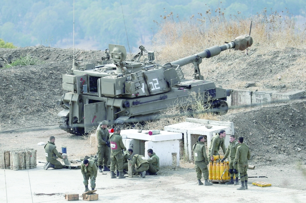 Israeli soldiers stand next to an artillery unit on the Israeli side of the border with Lebanon. - Reuters