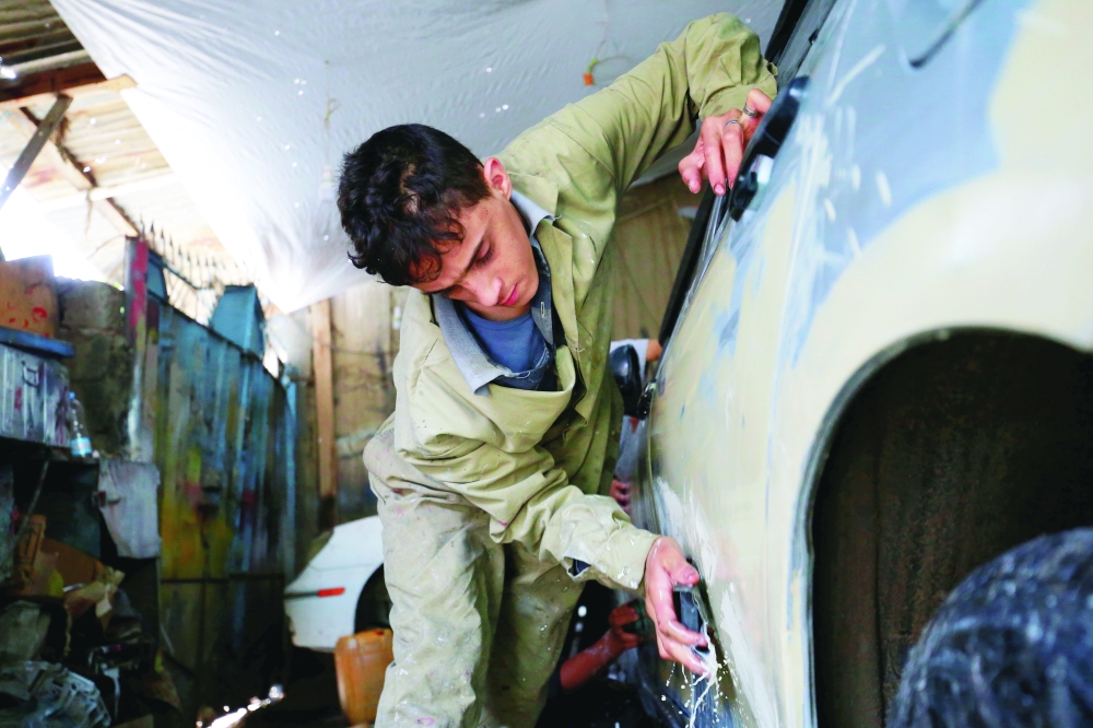 Boy sands the body of a car at an automotive body repair workshop in Sanaa. -- Reuters