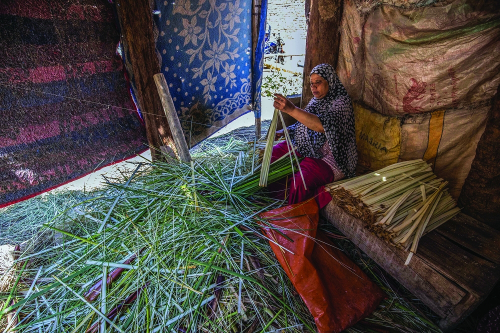 
TOPSHOT - A woman uses a thread to slice papyrus into thin strips at the workshop in the village of al-Qaramous in Sharqiyah province, in Egypt's northern fertile Nile Delta region, northeast of the capital, on July 28, 2021. In the lush green fields of Egypt's fertile Delta Valley, farmers in the small village of In the lush green fields of Egypt's fertile Delta Valley, farmers in the small village of Al-Qaramus have kept alive the ancient Pharaonic tradition of making papyrus paper. In the 1970s, a plastic arts teacher taught the farmers how to reappropriate agricultural and artistic techniques dating back millenia to plant the valuable reed and transform it into brownish paper with ornate drawings and text. Al-Qaramus is now the largest hub of papyrus production nationwide, according to agricultural experts.