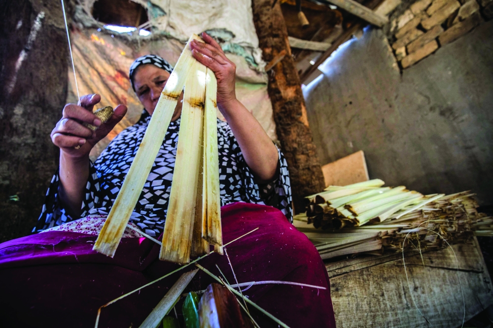A woman cuts papyrus by a thread at the workshop in the village of al-Qaramous in Sharqiyah province, in Egypt's northern fertile Nile Delta region, some kilometres northeast of the capital on July 28, 2021. In the lush green fields of Egypt's fertile Delta Valley, farmers in the small village of In the lush green fields of Egypt's fertile Delta Valley, farmers in the small village of Al-Qaramus have kept alive the ancient Pharaonic tradition of making papyrus paper. In the 1970s, a plastic arts teacher taught the farmers how to reappropriate agricultural and artistic techniques dating back millenia to plant the valuable reed and transform it into brownish paper with ornate drawings and text. Al-Qaramus is now the largest hub of papyrus production nationwide, according to agricultural experts.