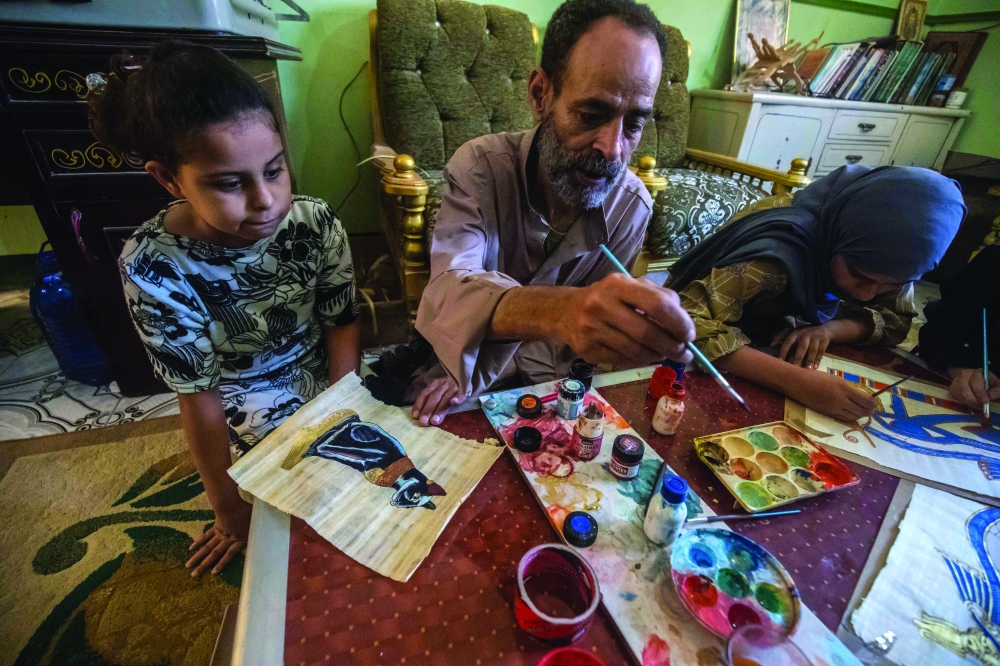 Farmer and painter Said Tarakhan, 60, draws on papyrus sheets at home in the village of al-Qaramous in Sharqiyah province,  in Egypt's northern fertile Nile Delta region, northeast of the capital, on July 28, 2021. In the lush green fields of Egypt's fertile Delta Valley, farmers in the small village of In the lush green fields of Egypt's fertile Delta Valley, farmers in the small village of Al-Qaramus have kept alive the ancient Pharaonic tradition of making papyrus paper. In the 1970s, a plastic arts teacher taught the farmers how to reappropriate agricultural and artistic techniques dating back millenia to plant the valuable reed and transform it into brownish paper with ornate drawings and text. Al-Qaramus is now the largest hub of papyrus production nationwide, according to agricultural experts.