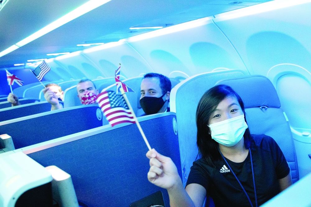 Passengers wearing protective masks hold American and British flags before a JetBlue flight to London at JFK International Airport. - Reuters 